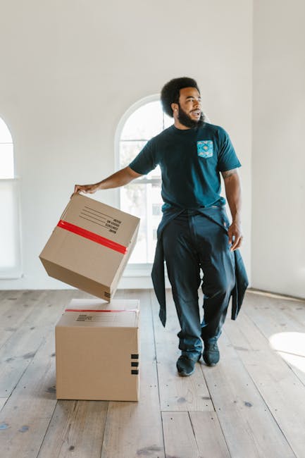 A person wearing a white shirt and light trousers is in an indoor setting, handling a medium-sized cardboard box as part of a home relocation process. They are seen lifting or positioning the box on t